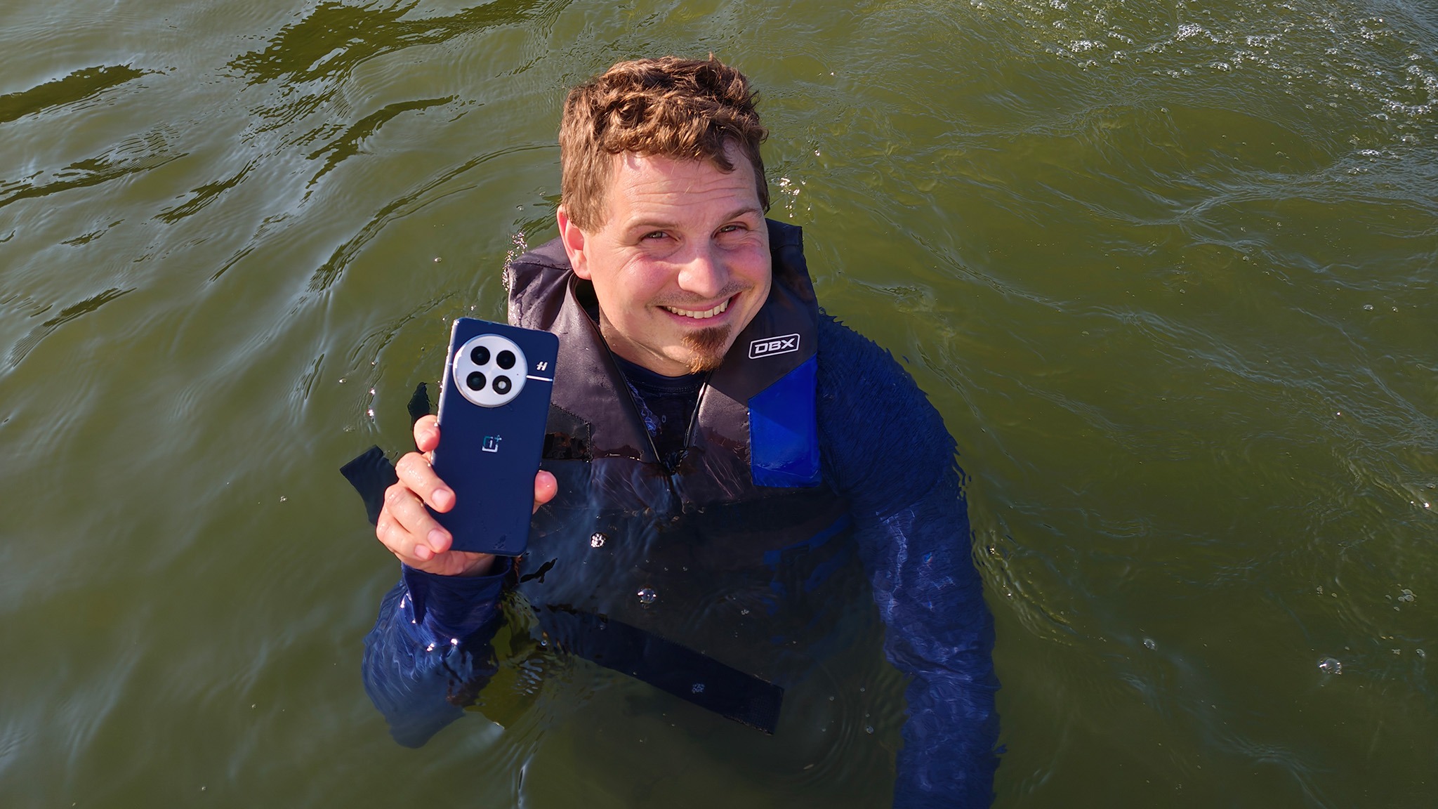 Holding a blue OnePlus 13 while floating in a lake